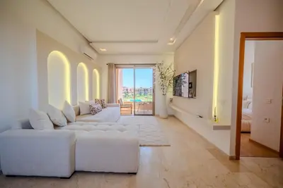 a living room with white furniture and a large window at Prestigia Apartment Secure Residence Pool in Marrakech
