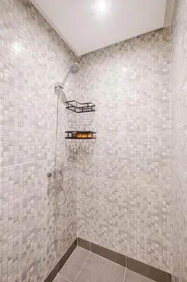 a shower in a white tiled bathroom with a shower head at Airport RAK 2Br perfect for early & late flights in Marrakech