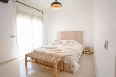 a white bedroom with a bed and a bench at Séjour confort jacuzzi et terrasse à Targa in Marrakech