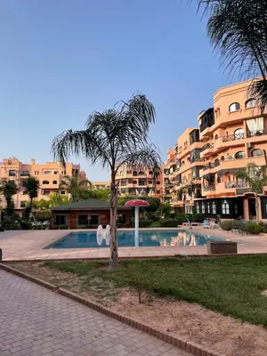 a palm tree in front of a building with a swimming pool at Premium Village, appartement cosy in Marrakech