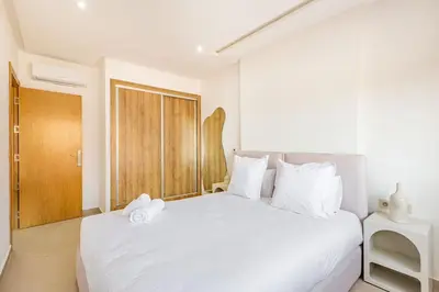 a bedroom with a white bed with a wooden door at Appartement chic près de la gare in Marrakech