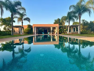 a swimming pool in front of a house with palm trees at Villa Serenity Marrakech in Châba