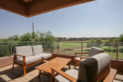 a balcony with chairs and a table and a view of a golf course at Saphire Luxury - Marrakech- Prestigia in Marrakech