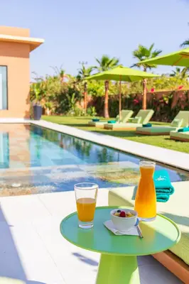 a drink and bowl of fruit on a table next to a swimming pool at Villa Jamila Marrakech in Segraga