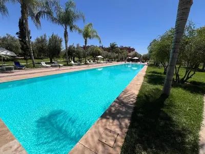 a swimming pool with blue water and palm trees at Appartement de charme au Vizir Resort in Dar Caïd Layadi