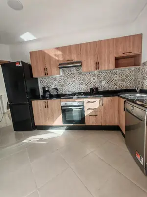 a kitchen with wooden cabinets and a black refrigerator at Elegant Apartment with King-Size Bed, Premium Amenities, 5 Pools & Free Parking in Marrakech