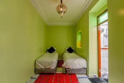 two beds in a room with green walls and a chandelier at Dar Tbib in Marrakech