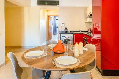 a dining room table with chairs and a red kitchen at Cocon de Guéliz - Central & balcon in Marrakech