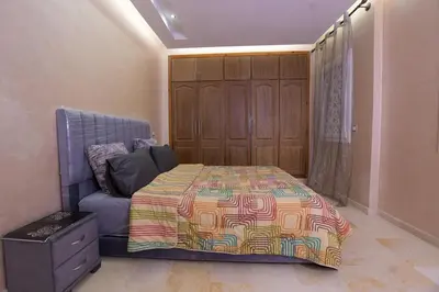 a bedroom with a bed and a chair and a cabinet at Appartement calme avec piscine et parking in Marrakech