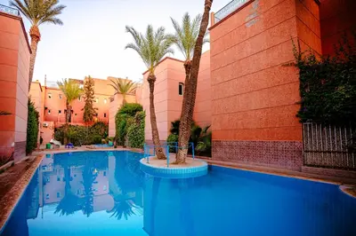 a swimming pool with palm trees next to a building at Riad 3ch, proche Médina, résidence avec piscines in Marrakech