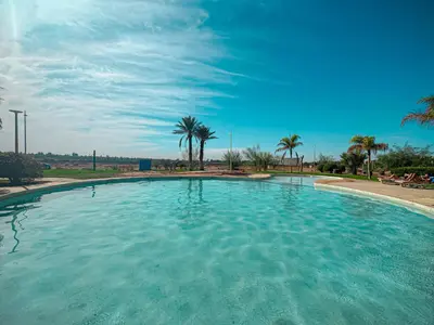 a large pool of blue water with palm trees at Palmeraie, Appart chic Suite & Accès à 3 Piscines in Dar Caïd Layadi