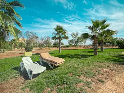 two chairs and a table in a park with palm trees at Palmeraie, Appart chic Suite & Accès à 3 Piscines in Dar Caïd Layadi