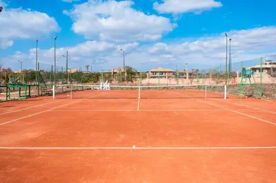 a tennis court with a net on a clay court at Palmeraie, Appart chic Suite & Accès à 3 Piscines in Dar Caïd Layadi