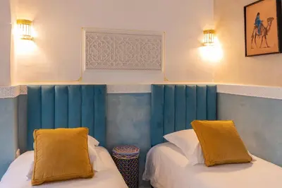 two beds in a room with blue walls and yellow pillows at Palais el Abbassia in Marrakech