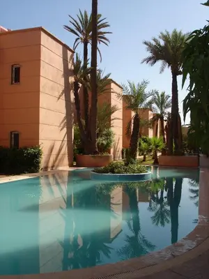 a swimming pool with palm trees and a building at Riad Nora - Confort, Calme & Sécurité in Marrakech