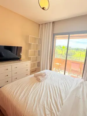 a bedroom with a bed and a television and a balcony at Appartement Confortable Vus Sur Piscine A Prestigia in Marrakech