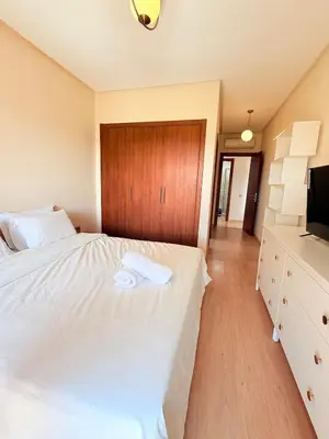 a bedroom with a large white bed and a television at Appartement Confortable Vus Sur Piscine A Prestigia in Marrakech