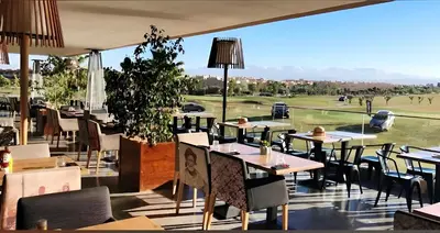 a restaurant with tables and chairs and a view of a golf course at prestigia urbane appartement marrakech in Marrakech