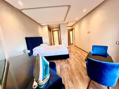 a room with a bed and a tv and chairs at Red nelbrj appartement in Marrakech