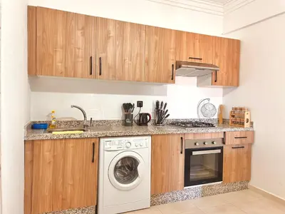 a kitchen with wooden cabinets and a washing machine at Appartement Chic près M Avenue Piscine Balcon in Marrakech