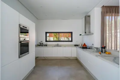 a white kitchen with white cabinets and a window at Villa LUMA - Akenza Residence in El Rhechat