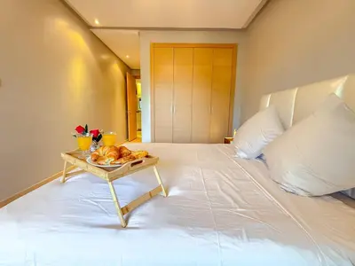 a white bed with a tray of food on a table at VIVASTAY Marrakech - Prestigia Topaze- Terrace overlooking garden & pool in Marrakech