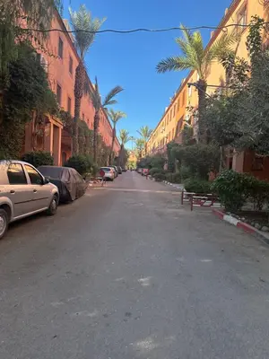 an empty street with parked cars and palm trees at Studio tranquille dans le village touristique in Marrakech