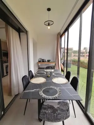 a dining room with a table and chairs and windows at Marrakech Noria Golf, cosy appartement 2 chambres in Marrakech