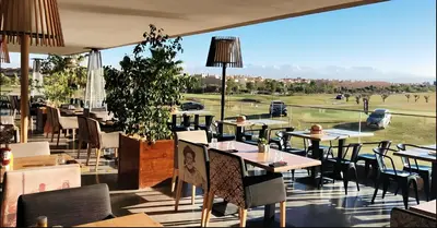 a restaurant with tables and chairs and a view of a golf course at Luxury Villa Private Pool & Golf View 7 min to center in Marrakech