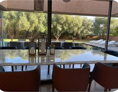 a glass table with chairs and a table with trees at Villa Brin d'Olive Marrakech 6 chambres in Gzoula