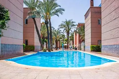 a large blue swimming pool with palm trees and buildings at appartement en résidence in Marrakech