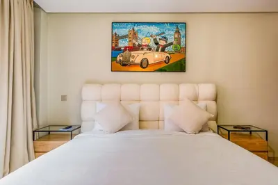 a bedroom with a white bed with a painting above it at Appartement Deluxe 2 chambres GUELIZ, Piscines, Spa, Gym in Marrakech