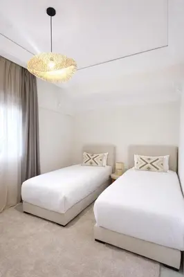 two beds in a white room with a chandelier at Luxury 2 Bedroom Apartment Pool & Garden Wifi in Marrakech