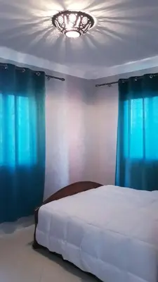 a bedroom with a bed with blue curtains and a chandelier at Beautiful apartment 5' from Macdonald, 10' from Downtown in Marrakech