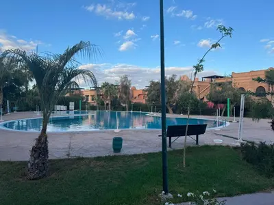 a swimming pool in a park with a bench and a palm tree at Appartement atlas golf ressort in Marrakech