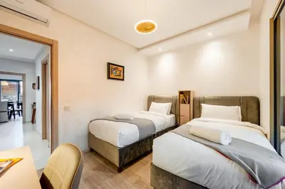 a hotel room with two beds and a table at Sunny Luxe 2BR Heaven Apt Wi-Fi, Balcony & Pool in Marrakech
