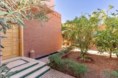 a brick building with a wooden door and trees at Villa Akenza piscine privée Marrakesh in El Rhechat