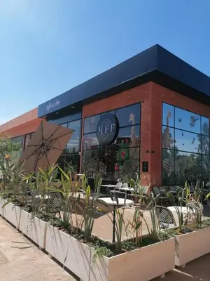 a cafe with tables and umbrellas in front of a building at Appartement 2 chambres avec grand jardin Noria Golf in Marrakech