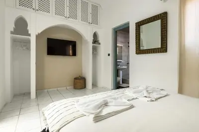 a white bedroom with a bed with a mirror at Riad Qarya Petit-déjeuner et transfert inclus in Marrakech