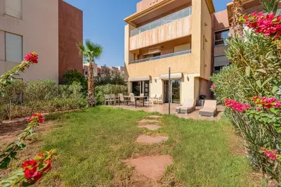 a yard in front of a building with pink flowers at Prestigia Agate Appartement luxueux Marrakech golf city in Marrakech