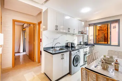 a kitchen with white cabinets and a sink and a table at Appartement chic et confortable au cœur de Gueliz in Marrakech