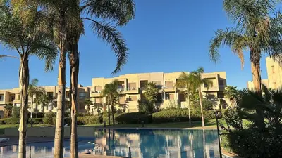 a building with palm trees in front of a pool at La Perle de Marrakech in Marrakech