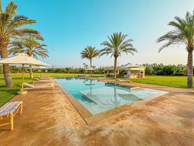 a swimming pool with palm trees and a house at Private Mountain View Oasis in Bou Azza