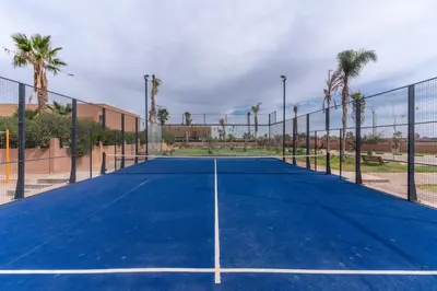 a tennis court with a net and palm trees at Luxury Villa with Breakfast & Padel Access in Marrakech