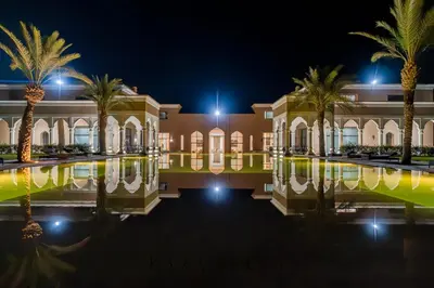 a building with palm trees and a pool at night at KAZA BELLA - Palais Les Orchidées in Marrakech