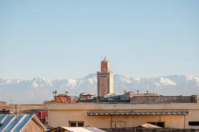 a city with a clock tower with mountains in the background at Riad Bahia Burgos - Exclusive - Heated Pool & Breakfast - 15 min walk Jemaa El Fnaa in Marrakech