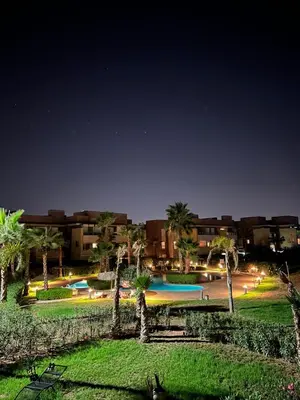 a park with a pool and palm trees at night at Appart Essalam 2 in Marrakech