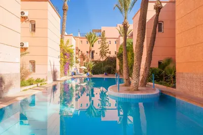 a swimming pool with palm trees and a building at Elegant 3-Bedroom Duplex with Pool in Marrakech