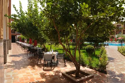 a restaurant with tables and chairs under a tree at Ennakhil Marrakech Hotel & SPA in Marrakech