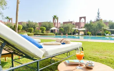 a bed and a drink on a table next to a pool at Les Jardins De Zyriab in Aït Hamid